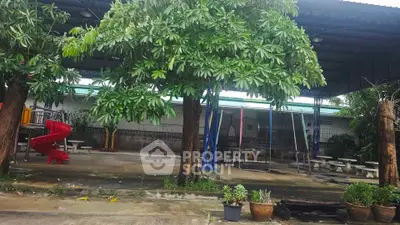 Spacious outdoor area with playground and seating under lush trees, perfect for family gatherings.