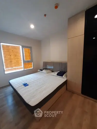 Modern bedroom with large bed and natural light from window, featuring sleek wooden flooring and built-in wardrobe.