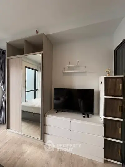 Modern bedroom with sleek wardrobe and TV unit, featuring stylish storage solutions and natural light.