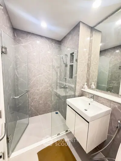 Modern bathroom with glass shower and sleek vanity in contemporary apartment.