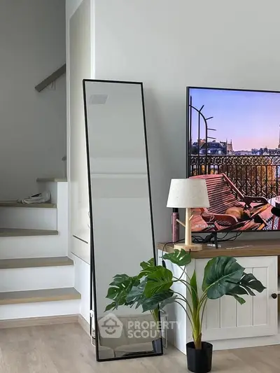 Modern living room with stylish decor, featuring a large mirror, TV, and indoor plant for a cozy ambiance.