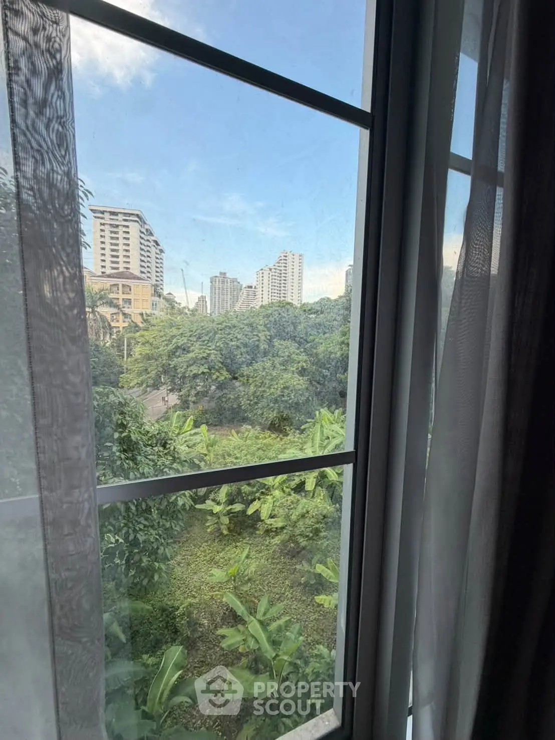 Stunning cityscape view from a window with lush greenery and urban skyline.
