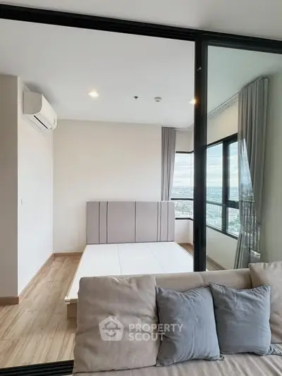 Modern bedroom with large windows and city view, featuring minimalist design and neutral tones.