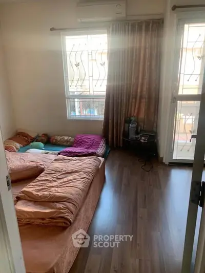 Cozy bedroom with wooden flooring and natural light, featuring a comfortable bed and balcony access.
