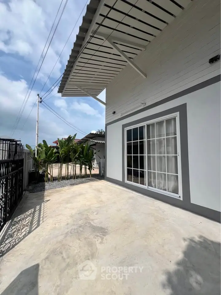 Modern house exterior with large sliding glass door and spacious concrete patio.