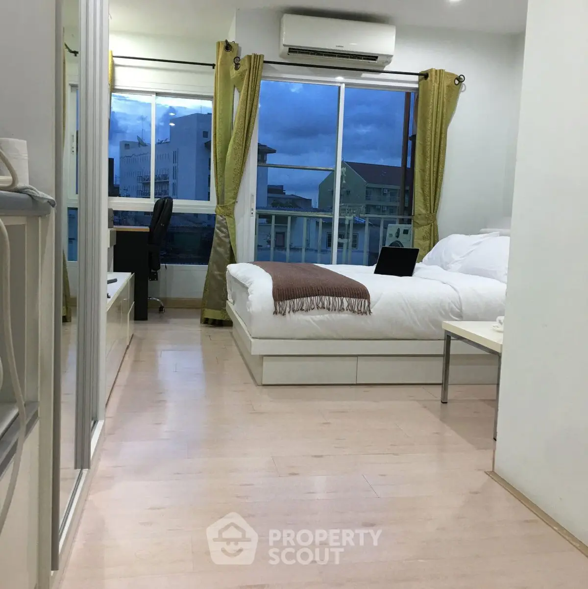 Modern bedroom with large window and city view, featuring sleek furniture and cozy ambiance.