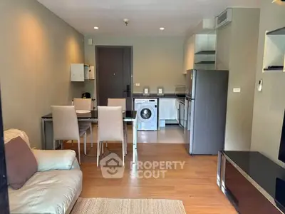 Modern open-plan living room with dining area and kitchen featuring a washing machine and sleek appliances.