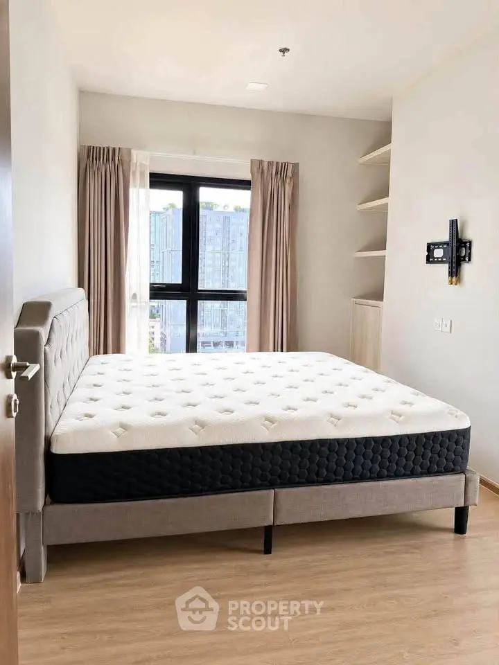 Spacious bedroom with large window and modern bed frame, offering natural light and city views.