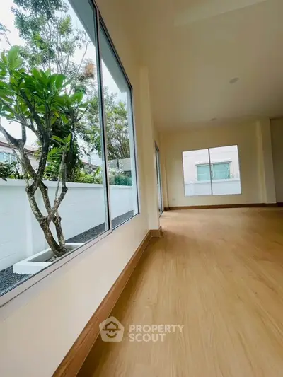 Spacious living room with large windows and garden view, featuring elegant wooden flooring.