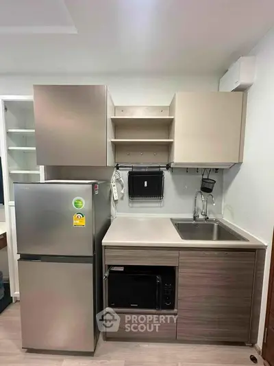 Modern compact kitchen with stainless steel fridge and microwave, sleek cabinetry, and efficient layout.