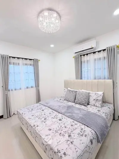 Elegant bedroom with plush bedding and modern decor, featuring a stylish chandelier and ample natural light.