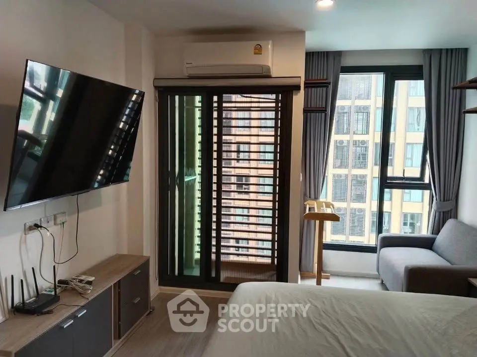 Modern bedroom with balcony access and city view, featuring a wall-mounted TV and stylish furnishings.