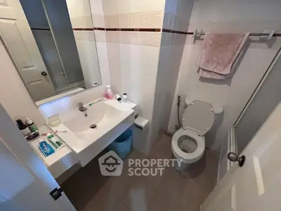 Compact bathroom with modern fixtures and white tiles, featuring a sink, toilet, and mirror.