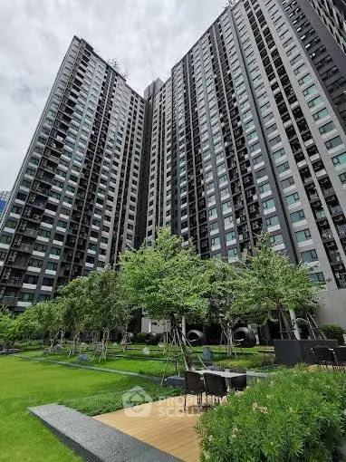 Modern high-rise building with lush garden and outdoor seating area.