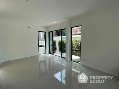 Spacious and bright living area with glossy tiled flooring, large windows offering ample natural light, and direct access to a serene outdoor view, perfect for modern living.