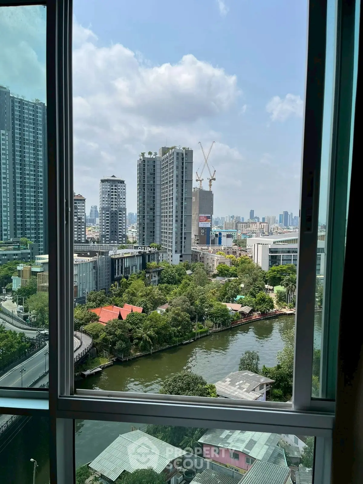 Stunning cityscape view from a high-rise window overlooking a serene canal and lush greenery.