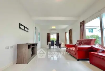Spacious living room with red leather sofas and dining area, featuring large windows for natural light.
