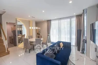 Modern living room with elegant blue sofa and dining area, featuring large windows and stylish lighting.