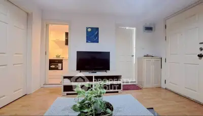 Cozy living room with TV and plant, adjacent to a modern kitchen.