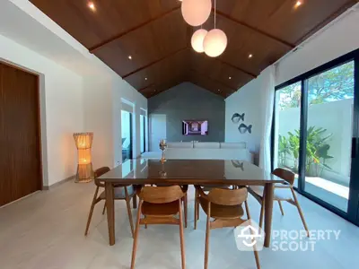 Elegant dining area with wooden ceiling and modern furniture, featuring large glass doors opening to a lush garden.