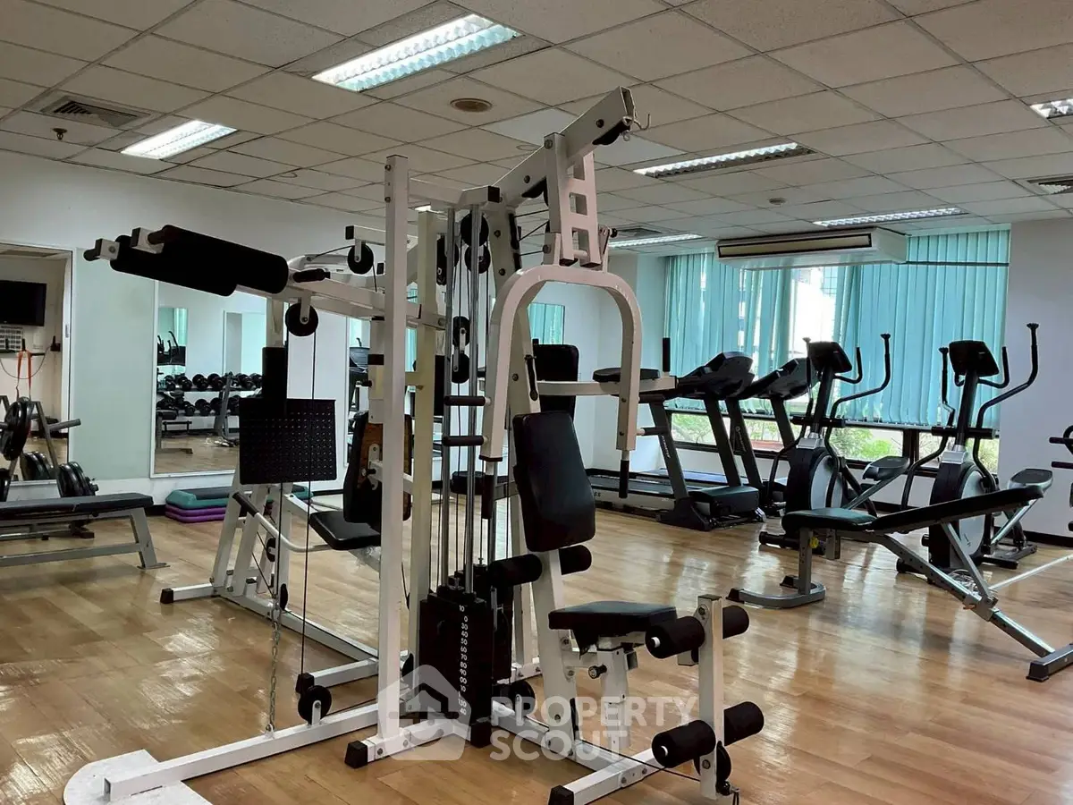 Spacious gym with modern equipment and wooden flooring in a well-lit room.