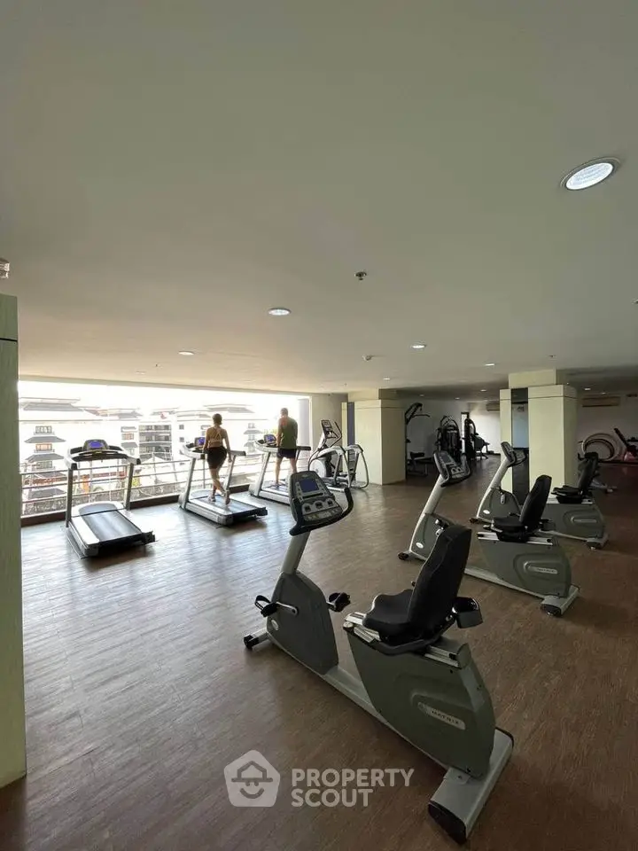 Spacious gym with modern equipment and city view in luxury apartment complex.