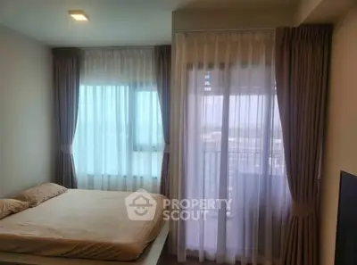 Cozy bedroom with large windows and balcony access, offering ample natural light and modern curtains.