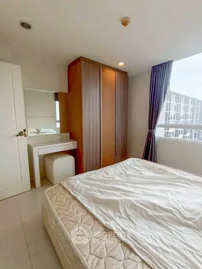 Bright bedroom with large window and modern furniture in a high-rise apartment.