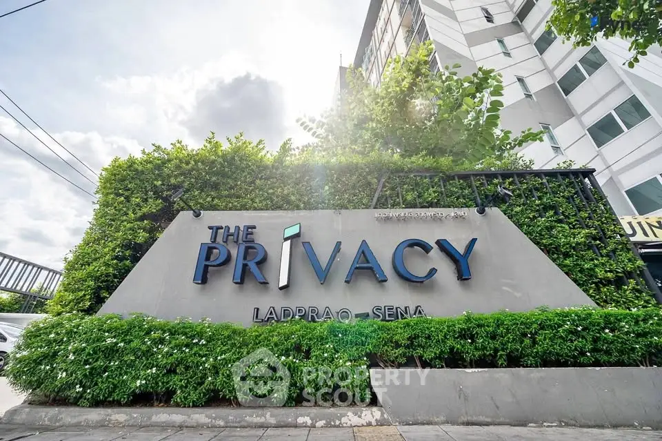 Modern condominium entrance with lush greenery and stylish signage at The Privacy Ladprao-Sena.