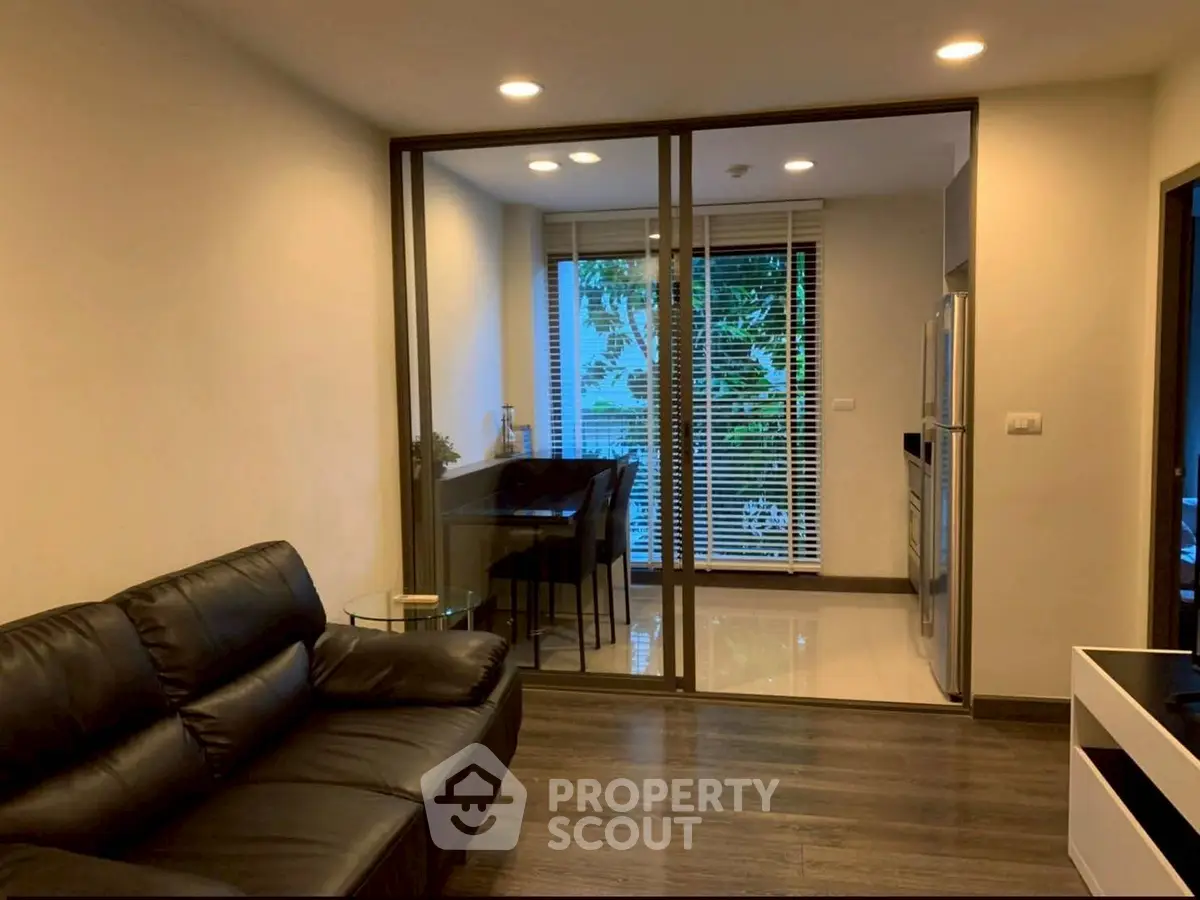 Modern living room with sleek black leather sofa and glass sliding doors leading to a bright dining area.