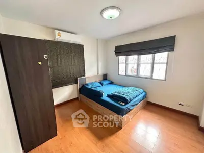 Cozy bedroom with wooden flooring, large window, and modern furnishings in a bright apartment.