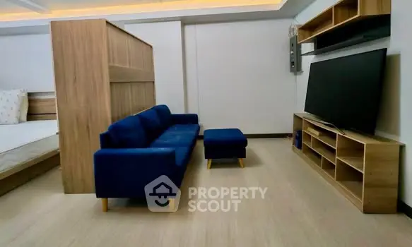 Modern living room with blue sofa, flat-screen TV, and wooden shelving in a stylish apartment.