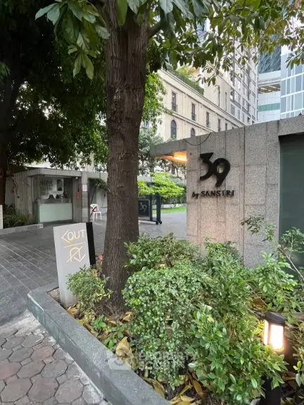 Elegant entrance of luxury residential building with lush greenery and modern design.