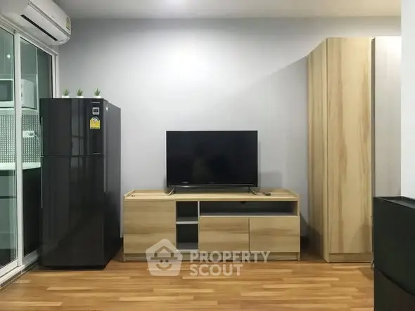 Modern living room with wooden flooring, sleek TV stand, and black refrigerator.