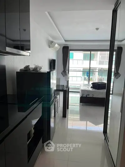 Modern studio apartment with sleek black kitchen cabinets and a cozy bedroom area, featuring large windows for natural light.