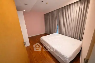 Spacious bedroom with wooden flooring and large window with curtains, perfect for relaxation.