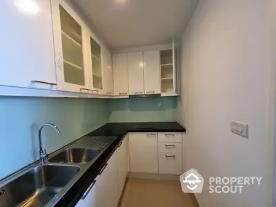 Modern kitchen with white cabinetry and black countertops, featuring a dual sink and ample storage space, ideal for culinary enthusiasts.