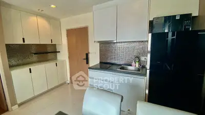 Modern compact kitchen with sleek cabinets and black fridge in cozy apartment.