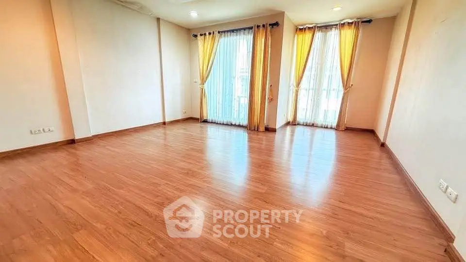 Spacious empty living room with wooden flooring and large windows with curtains.