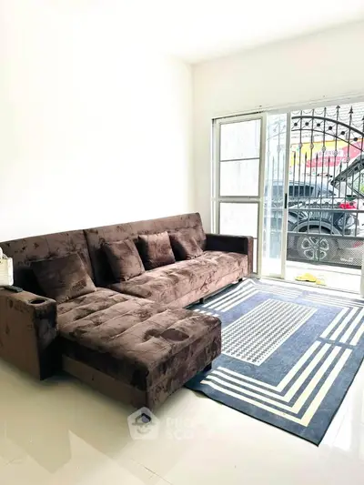 Spacious living room with plush brown sofa and modern rug, featuring natural light from large windows.