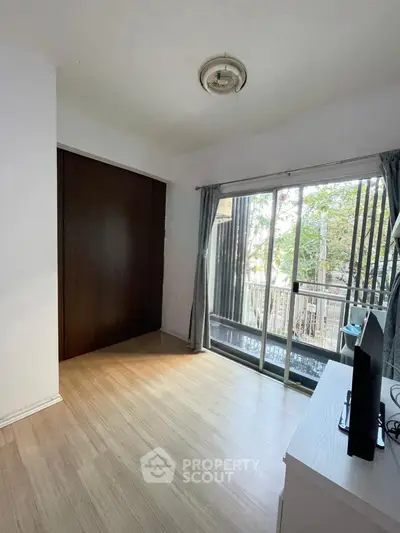 Bright bedroom with sliding glass doors leading to a small balcony, featuring wooden flooring and a built-in closet.