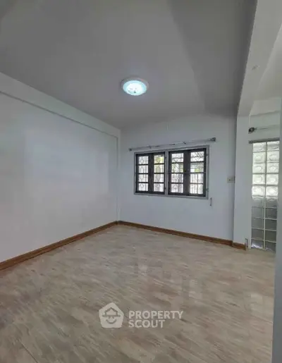 Spacious empty room with large window and wooden flooring, perfect for customization.