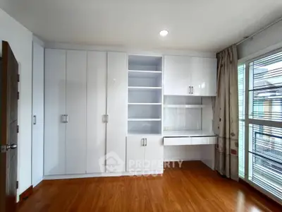 Spacious bedroom with built-in white wardrobe and desk, featuring large windows for natural light.