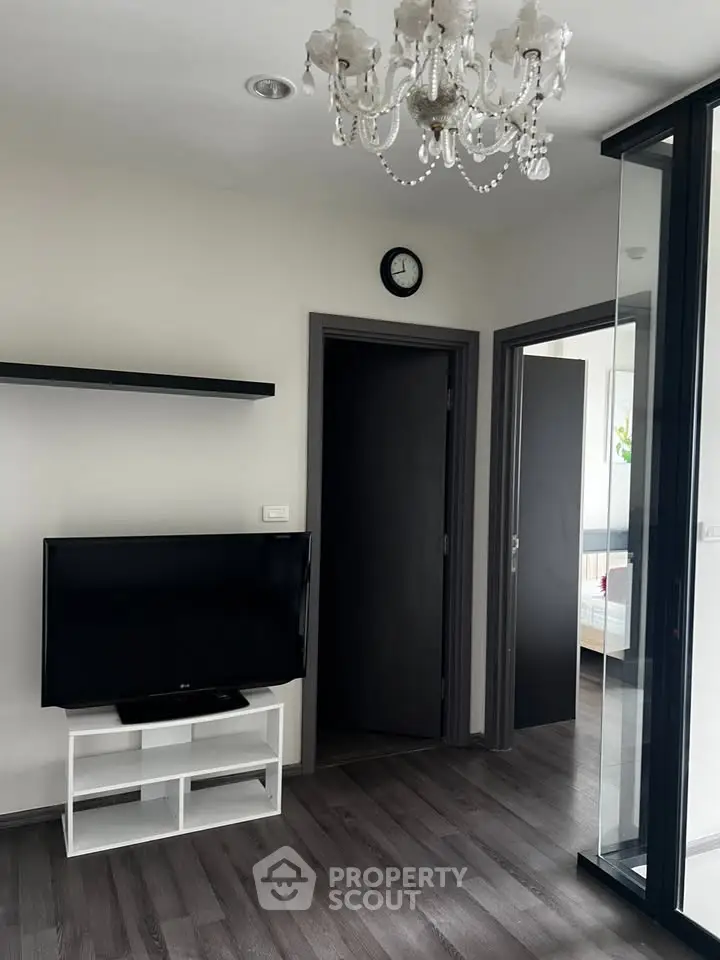Modern living room with chandelier and TV, featuring sleek flooring and glass partition.