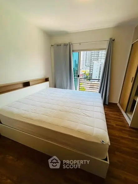 Bright bedroom with large window and city view, featuring a comfortable bed and wooden flooring.