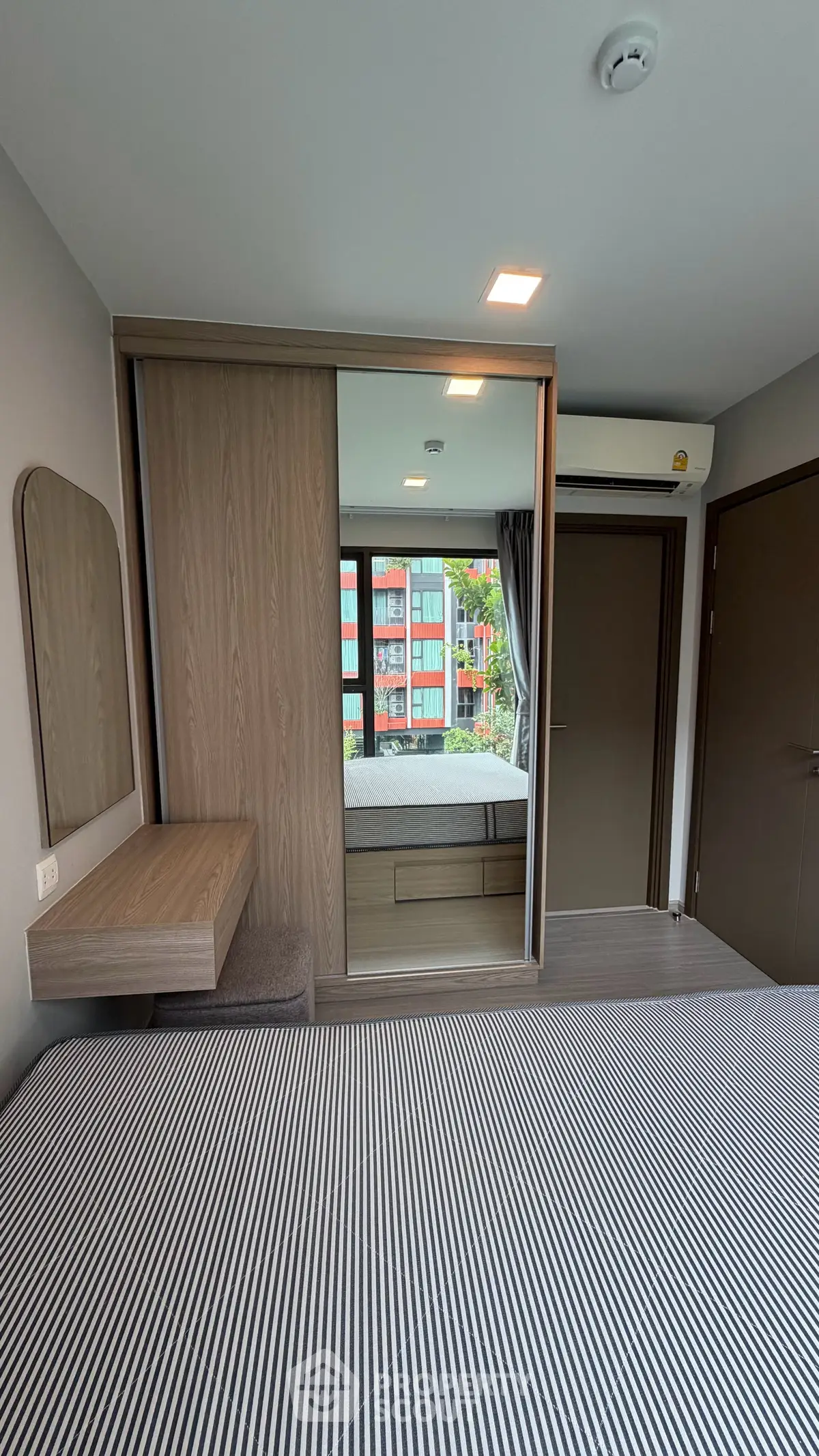 Modern bedroom with striped bedding, mirrored wardrobe, and large window view.