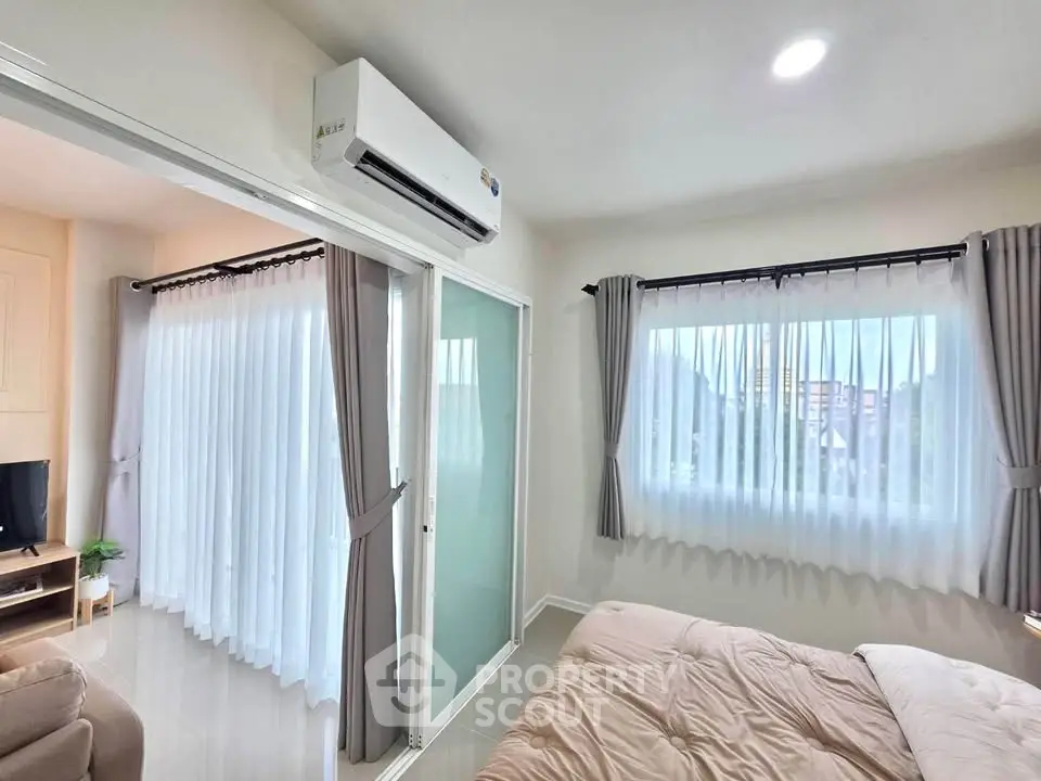 Bright and airy bedroom with large windows and modern air conditioning unit, perfect for comfortable living.
