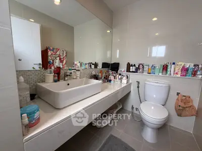 Modern bathroom with sleek sink and ample toiletries, showcasing contemporary design and functionality.
