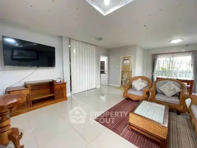 Spacious living room with modern TV setup and cozy wicker furniture, perfect for relaxation.