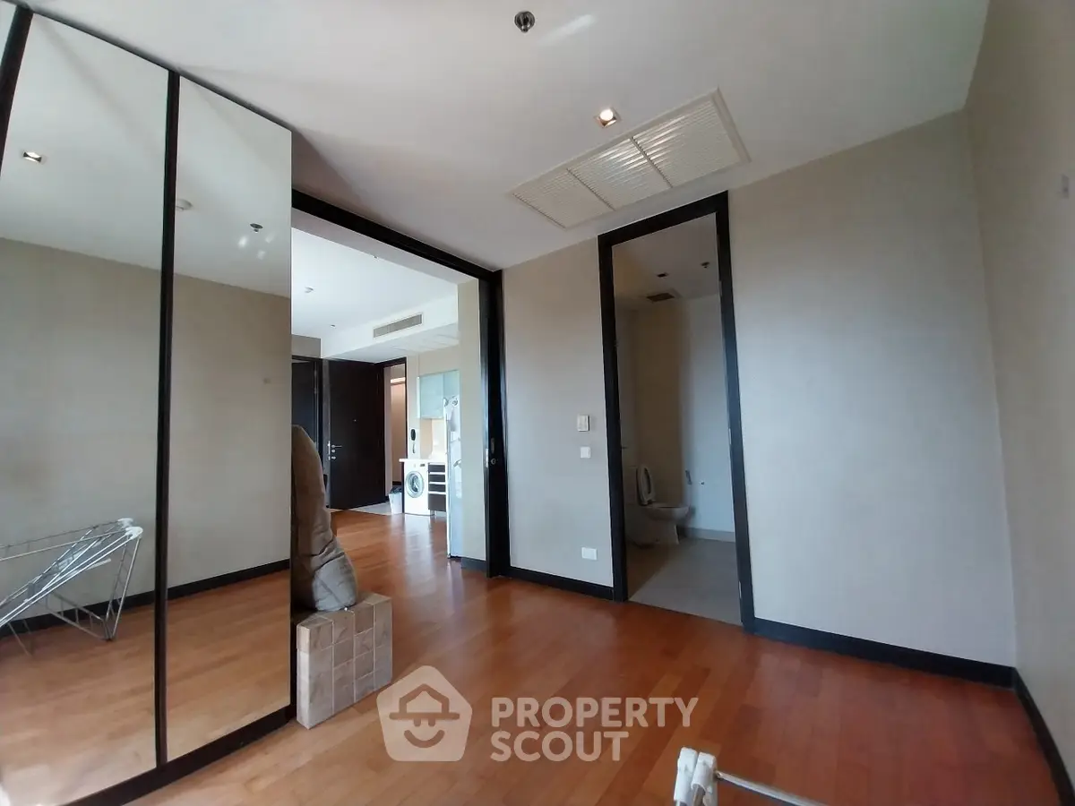 Spacious room with wooden flooring and mirrored closet doors, leading to a modern bathroom.